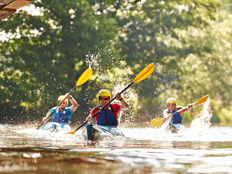 Eine Gruppe von Kanufahrern beim Paddeln auf einem Fluss nahe Bodenmais.